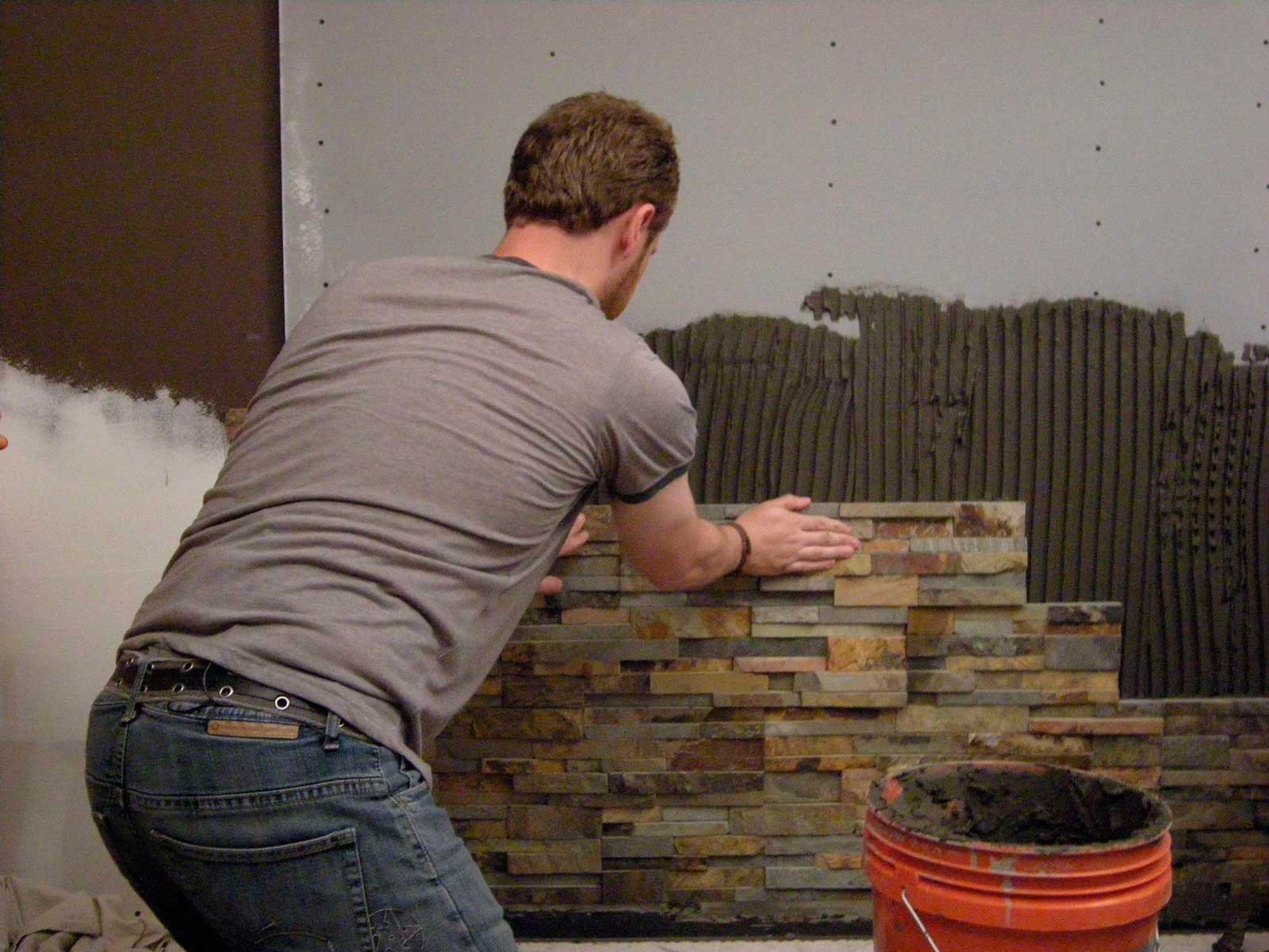 An installer setting stone veneer in a bathroom feature wall 